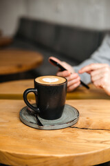Men's hands hold the phone. Communicate online on your smartphone. A man communicates online and drinks coffee in a coffee shop