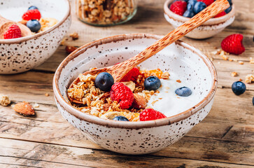 Healthy brakfast with yogurt and baked granola with berries in two small bowls, Granola baked with nuts, coconut oil and honey.