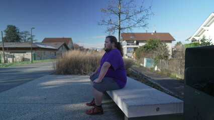 Fototapeta premium One young overweight man sitting at park bench outside. A contemplative person relaxing outdoors