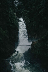 Fototapeta na wymiar Bridge over large waterfall in beautiful Canadian wilderness after rain in moody misty day