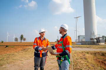 Two Caucasian engineers or technicians shake hands and stay in front of cluster of windmill or wind...