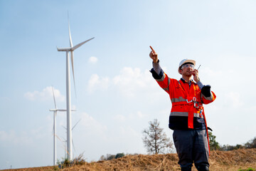 Engineer or technician worker use walkie talkie to contact and stand in front of windmill or wind turbine in concept of work with green ecology support power.