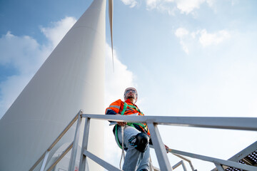 Caucasian engineer or technician walk down at base of windmill or wind turbine and look to right side and blue sky. © narong