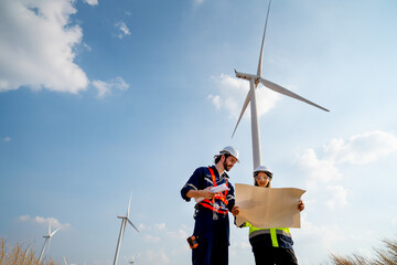 Lower view of Caucasian engineer or technician man and woman discuss together using drawing paper and stay in front of row of windmill or wind turbine with blue sky. © narong