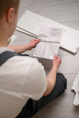 The furniture assembler is studying the instructions for assembling furniture, there are boards, screws nearby. Self-assembly of furniture. The concept of moving, repair. Close-up