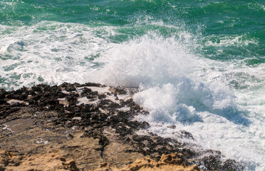 Fototapeta na wymiar Olas rompientes en la costa de Roca Vecchia en Lecce, Italia. Salpicaduras de las olas de un mar Adriático azul turquesa rompiendo contra los acantilados calizos en un soleado día de verano.