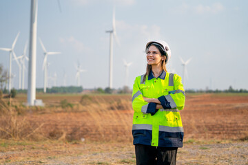 Pretty engineer woman with safety protection equipment stand with arm-crossed and look to left side stay in front of windmill cluster in the field.