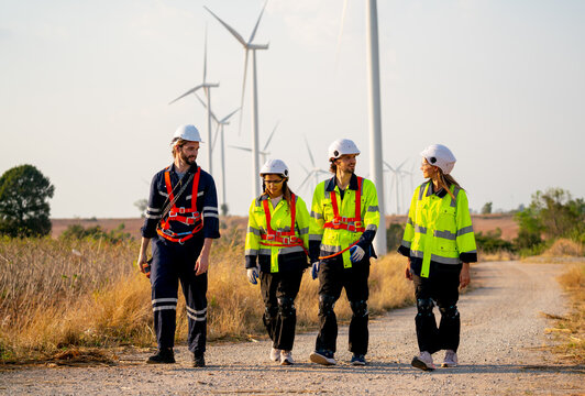 Group of engineer or technician man and woman walk along the road far from windmill or wind turbine and talk together after finish work.