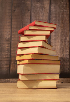 stack or column of red books forming a spiral and yellowish sheets of paper with dark wood background and light wood table vertical photo with space for text