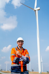 Engineer or technician worker stand in front of windmill or wind turbine and look at camera in concept of confidence and happiness to work with green ecology support power.