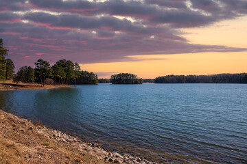 vast blue rippling water at Lake Lanier with the sun reflecting off the water and lush green trees with rocks along the banks and powerful clouds at sunset in Gainesville Georgia USA