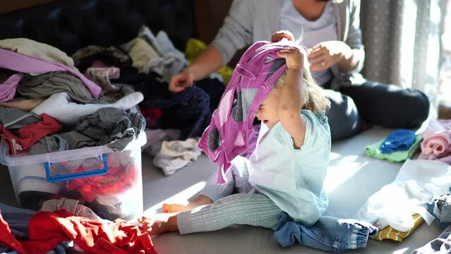 Little girl plays with the laundry that mom sorts on the bed