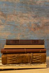 antique books and notebooks bound in leather with synthetic leather straps stacked on top of each other wooden table and blue wooden background vertical photo with space for text 