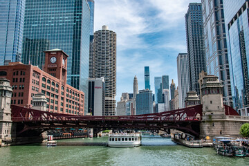 Fototapeta premium Tour Boat Going Under Bridge Along Chicago River With City Skyline in Background