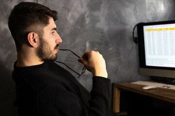 portrait d'un jeune employé de bureau ou homme d'affaires qui travaille devant son ordinateur. il réfléchit en mordillant ses lunettes