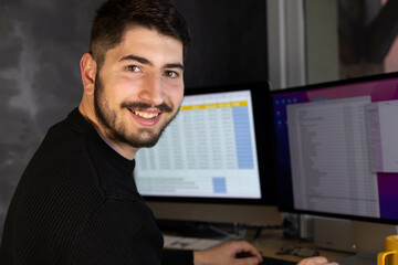 Fototapeta na wymiar portrait d'un jeune homme, étudiant ou employé de bureau souriant qui est assis devant son ordinateur. Il regarde la caméra.