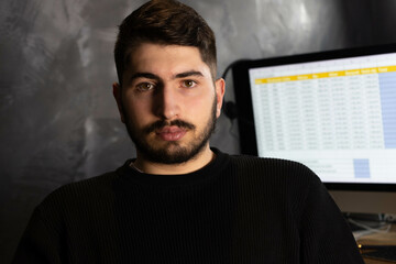 portrait d'un jeune homme, étudiant ou employé de bureau qui est assis devant son ordinateur. Il regarde la caméra.