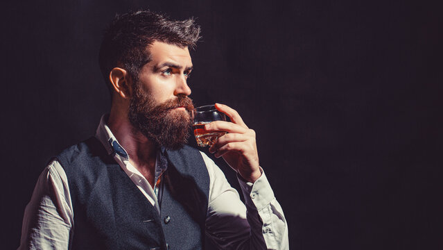 Sommelier tastes expensive drink. Bearded businessman in elegant suit with glass of whiskey