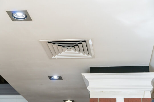 Suspended ceiling with built-in round LED lighting. Close-up of the details of the lamp and the grille of the air conditioner. Interior design, decorative moldings on the column. - Powered by Adobe