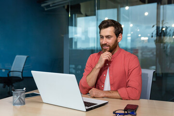 Portrait of a young male programmer, designer, freelancer in a red shirt who sits and works in the...