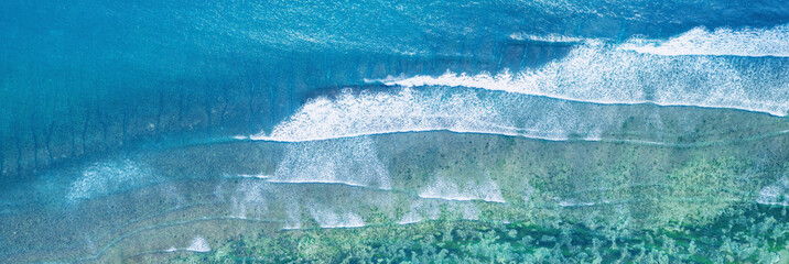 Scenic Aerial panoramic top down view at waves on wide very shallow calm shore with much sea grass, Sanur beach, Bali, Indonesia