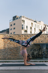 Vertical shot of a young woman performing yoga outdoors on her mat practicing the inverted asana posture by resting her forearms on the ground and raising her legs.