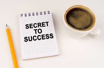 On a white surface, a cup of coffee, a pencil and a notepad with the inscription - SECRET TO SUCCESS