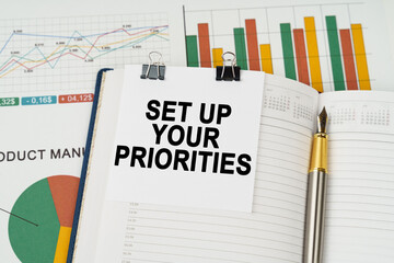 On the business charts is a notepad with the inscription - SET UP YOUR PRIORITIES