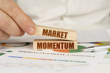 On the table are business charts and diagrams in the hands of a wooden block with the inscription - MARKET MOMENTUM