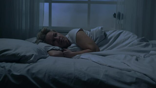 Woman suffering from insomnia at night lying in bed, sleep disturbance, sad pensive look, top view.