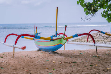 Colorful traditional Balinese boat taken from water on a Sanur beach in Bali, Indonesia. Boat under tree