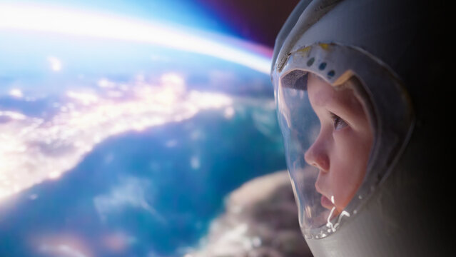 Little boy with an astronaut helmet looks at earth and sunrise in space from spaceship. Children's dreams of conquering space.