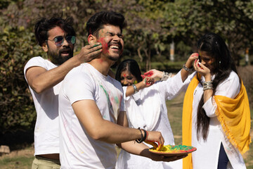 Friends family boys girls man woman celebrating enjoying holi festival of colors colours with gulal abeer color powder outdoor in a park, a popular hindu festival celebrated across india