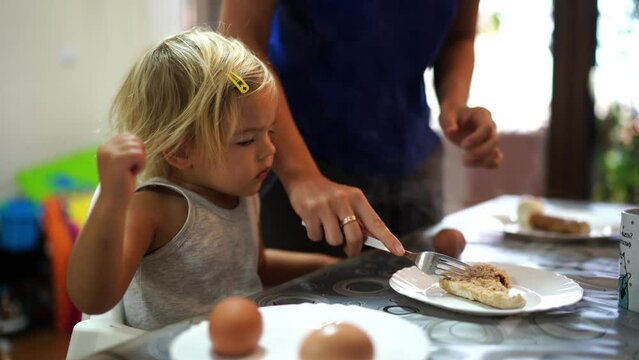 Mom kneads a cutlet in a plate with a fork in front of a little girl