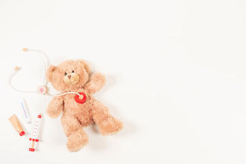 Teddy bear with toy stethoscope and wooden toy medicine tools on a white background. Top view. Concept of children's diseases, medicine, healthcare, medical insurance