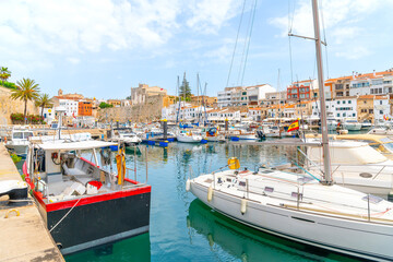 Boats line the picturesque marina port harbor at Ciutadella de Menorca, Menorca, Spain, in the Mediterranean Sea, with the historic town and  village in view.	