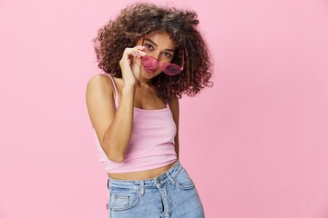 Happy woman with curly hair in a pink T-shirt and jeans on a pink background with sunglasses with a beautiful tan, DJ party, copy space