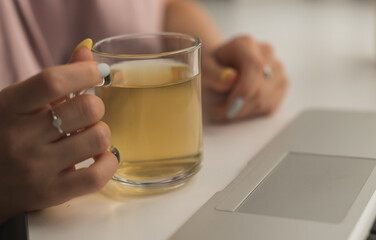 Female hands holding hot cup of tea close-up with laptop background