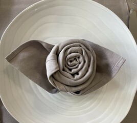 Napkin folded in the shape of a rose placed on a white plate with cutlery on each side