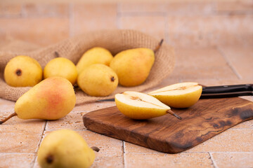 Fresh yellow pears on burlap and pear halves cut with a knife on a wooden olive board on a stone beige table