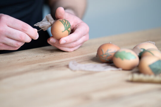 close up of male hands decorating easter eggs with different types of leaves. Interesting method for decorating easter eggs with leaves. Eggs decoration with leafs. Young man decorating easter eggs.