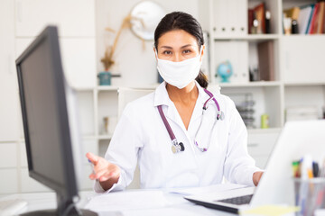 Female doctor in in protective medical mask working on laptop in clinic