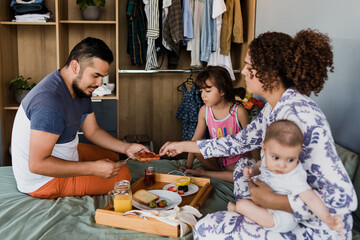 hispanic family husband with children bringing his wife breakfast in bed at home in Mexico Latin America