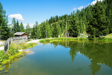 Fototapeta premium Mountain lake with children's playground in the background. Grafenberg Hill, Wagrain, Austria.