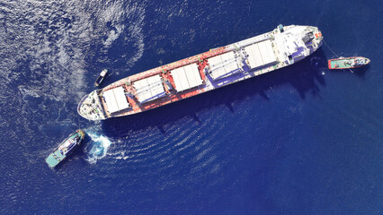 Aerial drone top down photo of super tanker towed by tug boat in deep blue sea near logistics...