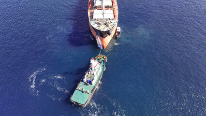 Aerial drone top down photo of super tanker towed by tug boat in deep blue sea near logistics...
