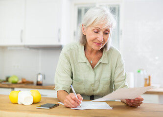 Cheerful old woman writing on paper, calculating bill payment.