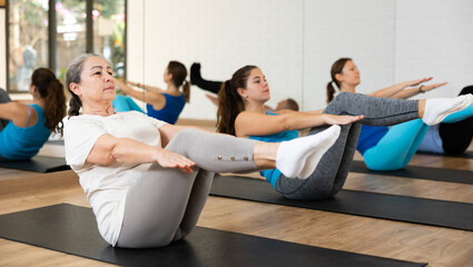 Concentrated sporty senior woman doing v-sit during bodyweight workout to strengthen abs and core muscles in fitness studio