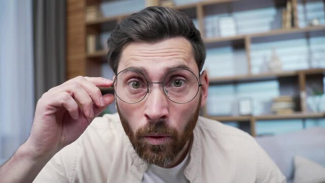Camera view of amazed shocked bearded man with glasses staring into camera demonstrates wow surprised face expression indoors Happy male rejoices by sudden incredible news promotion sale at home 