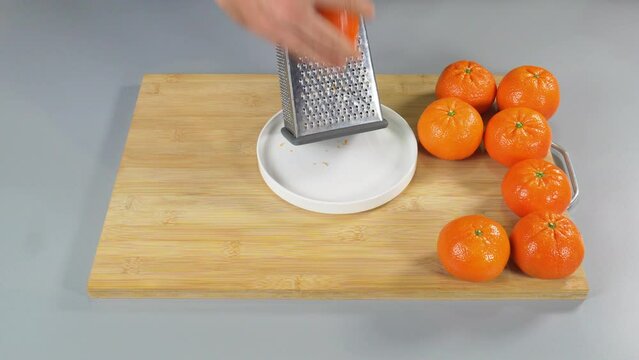 A man rubs the peel of a mandarin citrus on a grater. Folds the zest. High quality 4k footage